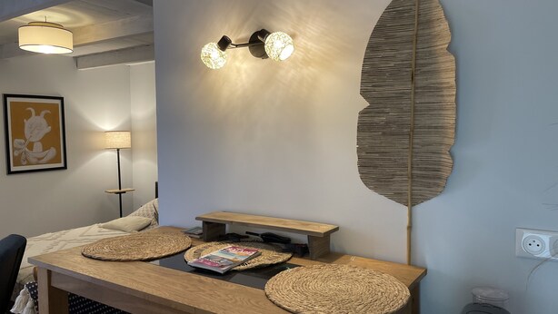 Una habitación moderna con una mesa de madera, individuales tejidos, una revista, una lámpara y luces en la pared.