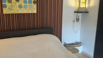 Una cama bien hecha con una cubierta blanca texturizada, una obra de arte colgada en la pared con un estampado de lunares y una lámpara de pared con pantalla decorativa.