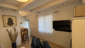 Una sala de estar con un sofá, un televisor montado en la pared y un comedor con mesa y sillas.