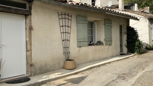 Un edificio con una puerta blanca, una planta en maceta y una ventana con contraventanas.