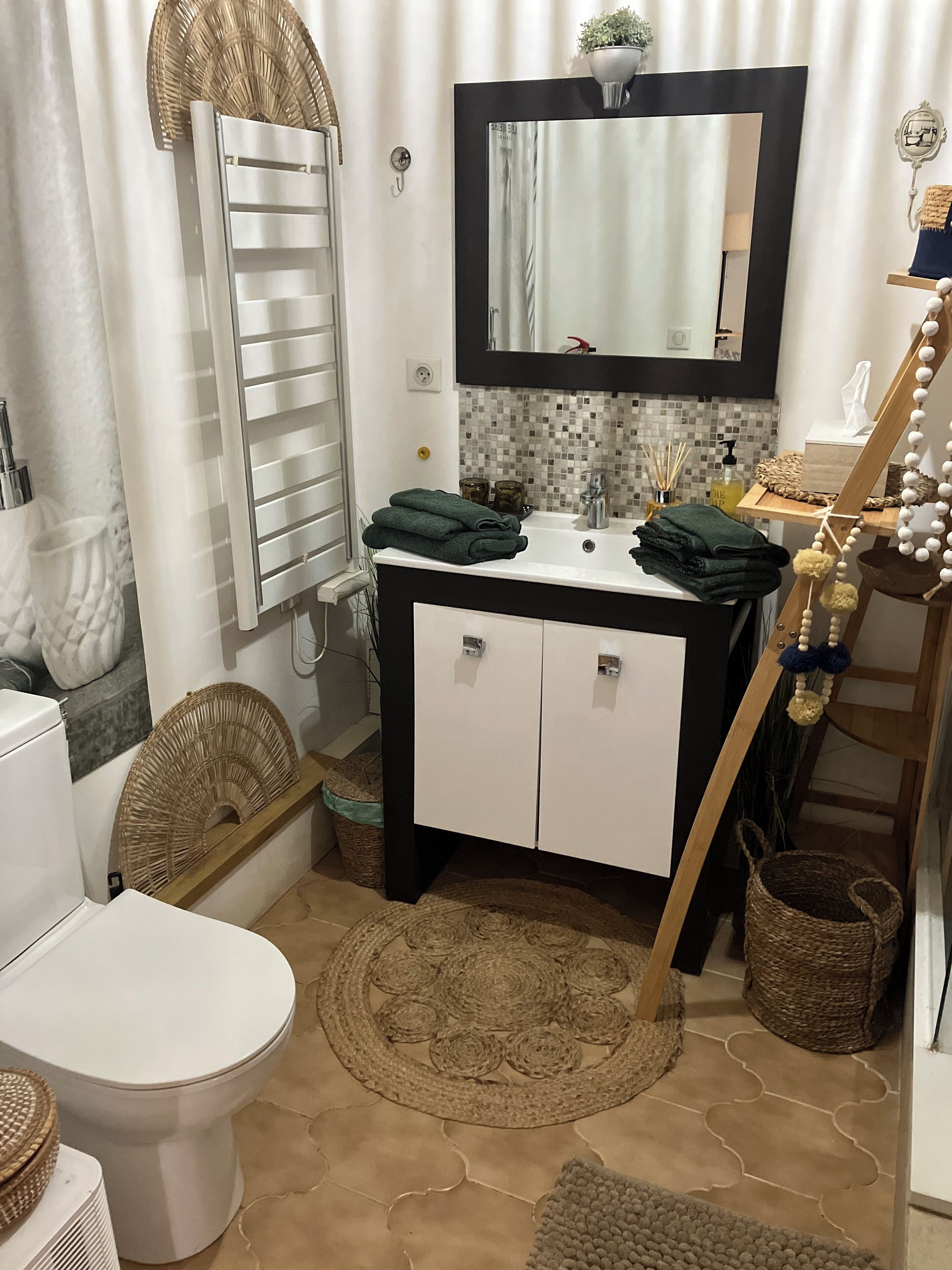 Un baño con inodoro blanco, un lavabo con espejo y un perchero para toallas.
