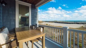 Eine überdachte Veranda mit einem Holztisch und Stühlen, einem weißen Geländer und Blick auf Strand und Meer.