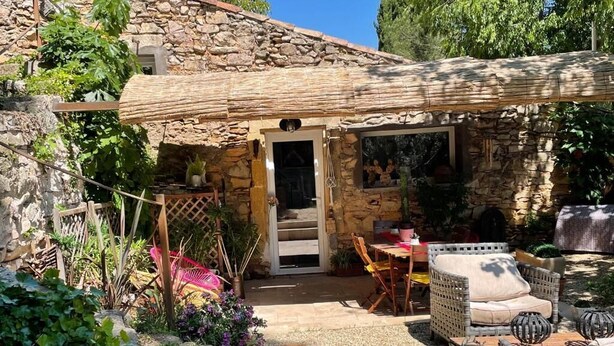 Una casa de pedra amb un porxo cobert, mobiliari exterior i un jardí.