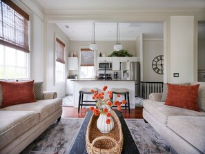 A living room with a sofa, a coffee table with a vase, and a kitchen in the background.