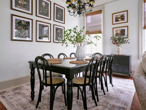 Ein Esszimmer mit einem rechteckigen Tisch, umgeben von Stühlen, Bildern an der Wand und einer Kandelaber.