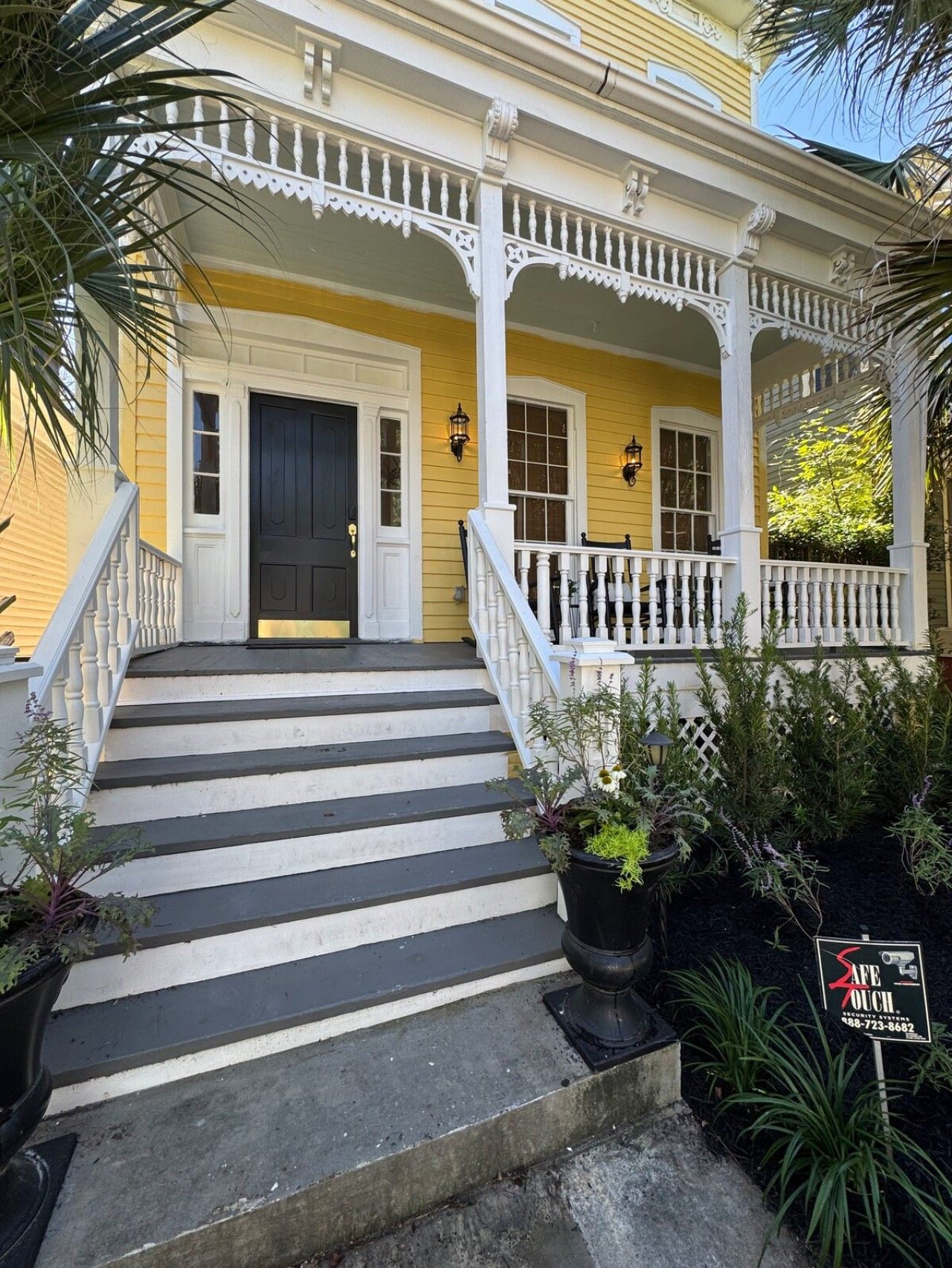 A yellow house with a white porch, black steps, and a black front door.