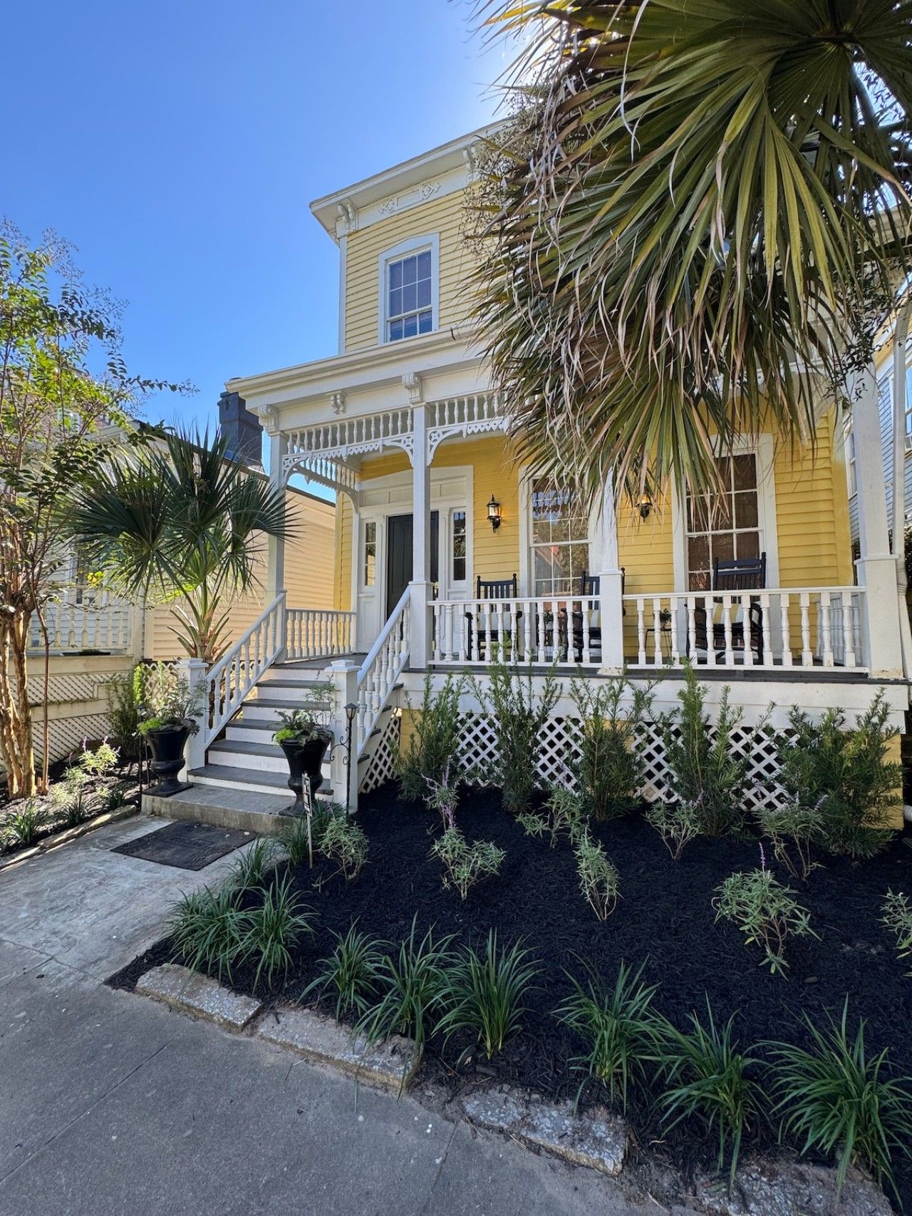 A yellow house with a porch, a staircase, and a garden with various plants.