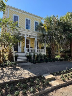 A yellow house with a white porch and steps leading to the entrance.