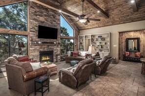 A spacious living room with a stone fireplace, leather furniture, and a large TV mounted on the wall. -  "Mountain Escape," Our cozy mountain home, Quiet Neighborhood (Alto)