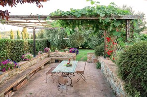 Une terrasse de jardin avec une table et des chaises, entourée de murs en pierre et agrémentée de diverses plantes.
