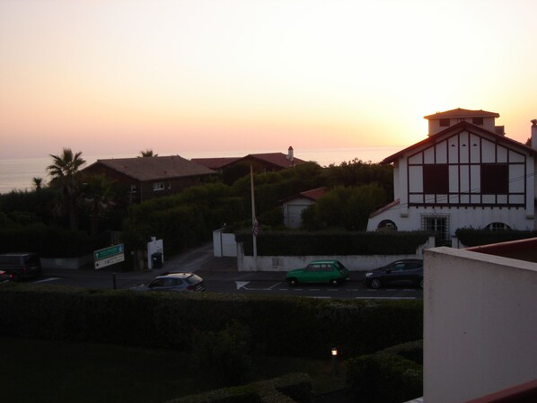 A coastal residential area with houses, a road, and parked cars during sunset.