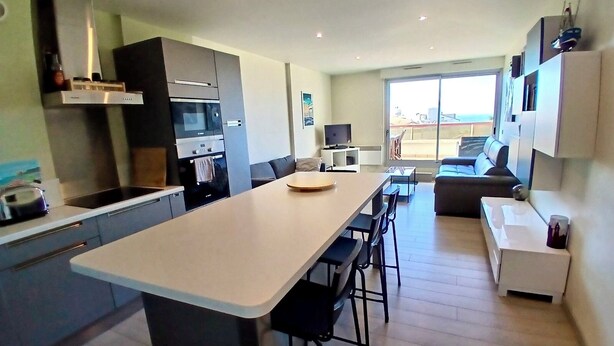 Een moderne keuken met een centraal eiland, inbouwapparatuur en een eethoek met barkrukken.