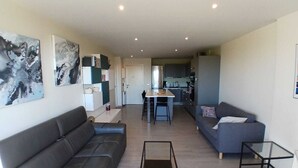 Een moderne woonkamer met een bank, een salontafel en een eethoek, met een keuken op de achtergrond.
