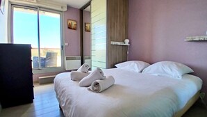 Een hotelkamer met een groot bed, een bureau en een glazen schuifdeur naar een balkon.
