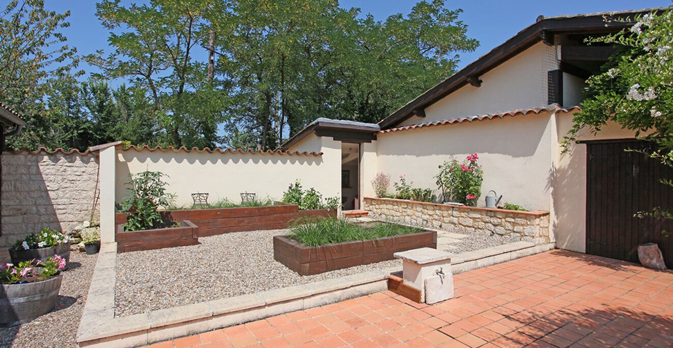 A courtyard with raised garden beds, a stone wall, and a tiled patio.