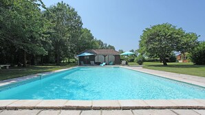 A rectangular swimming pool with a tiled deck, surrounded by trees and a building with a tiled roof. - Character cottage, large garden and swimming pool, tranquility guaranteed (Sérignac-Péboudou)