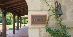 Un mur de pierre sur lequel est fixée une plaque portant l’inscription « CHAUPRADES » et une cloche.