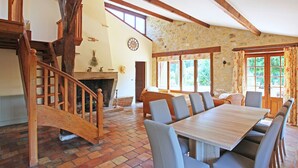 A spacious dining area with a large wooden table and modern chairs, a stone fireplace, and a wooden staircase leading to an upper level. - Character cottage, large garden and swimming pool, tranquility guaranteed (Sérignac-Péboudou)