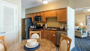 Cocina compacta con armarios de madera, un microondas y un refrigerador. Hay una mesa de comedor con sillas y un tazón encima.