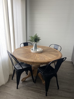 Una mesa de comedor redonda de madera con cuatro sillas negras, un florero blanco con una planta y una pizarra sobre la mesa.