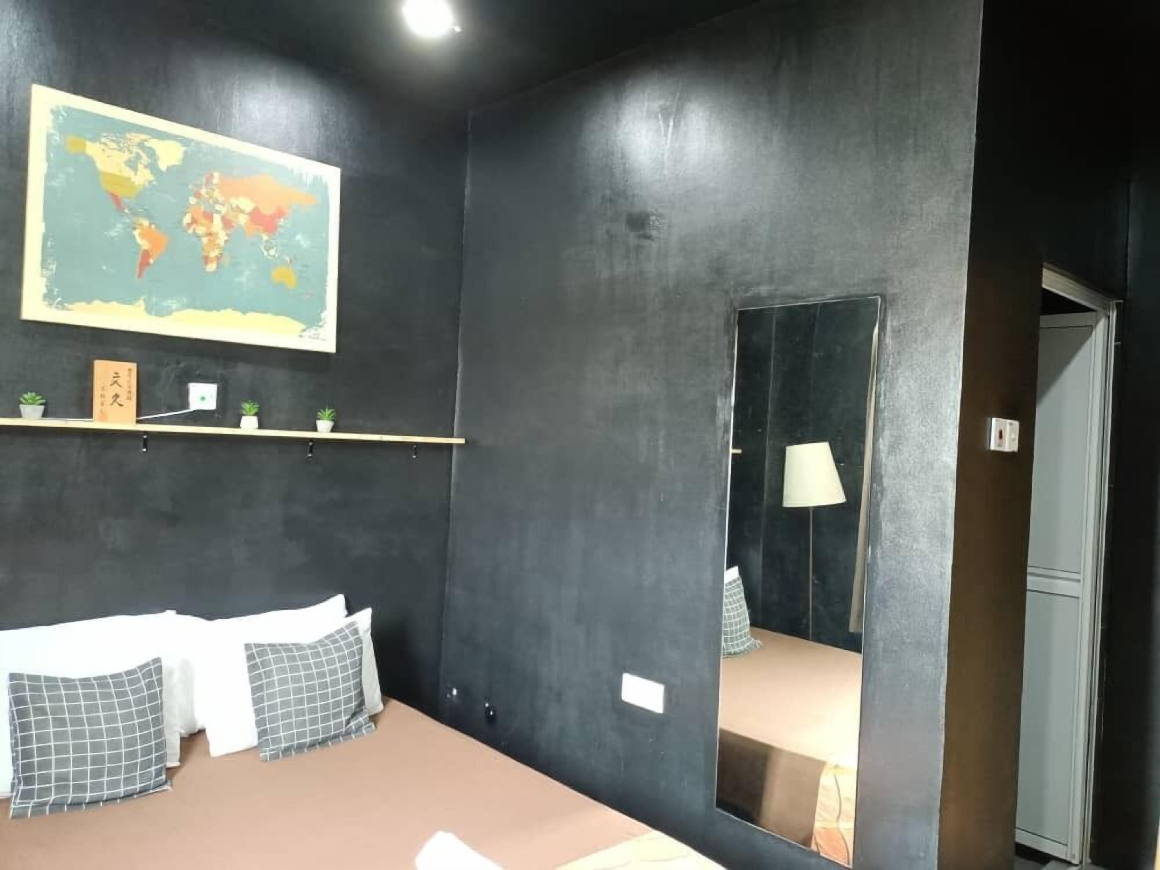 Un dormitorio con cama, almohadas, un mapa del mundo en la pared, una estantería con objetos pequeños y un espejo.