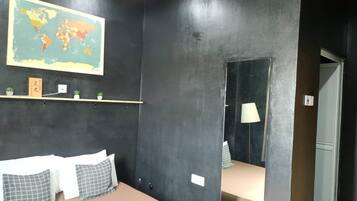 Un dormitorio con cama, almohadas, un mapa del mundo en la pared, una estantería con objetos pequeños y un espejo.