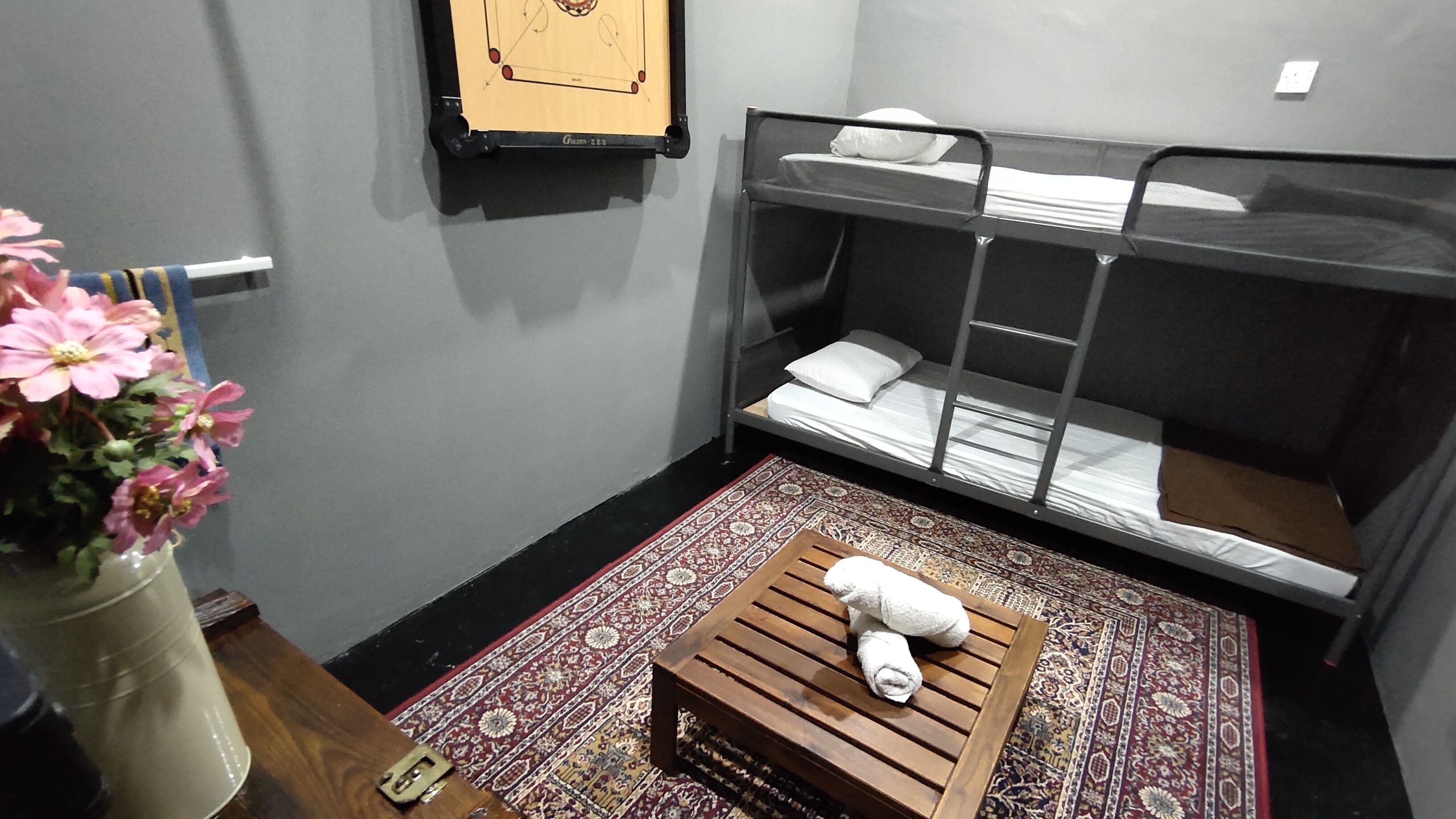 A room with bunk beds, a wooden crate with a towel, a patterned rug, and a wall-mounted board game.