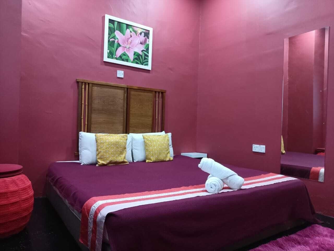 A room with a bed, pillows, a red round table, and a painting on the wall.