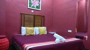 A room with a bed, pillows, a red round table, and a painting on the wall.