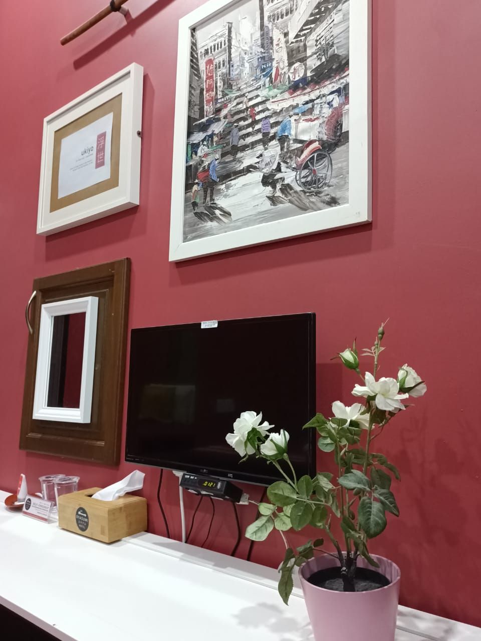 Una habitación con una pared roja, un cuadro enmarcado, un televisor y una planta en maceta.