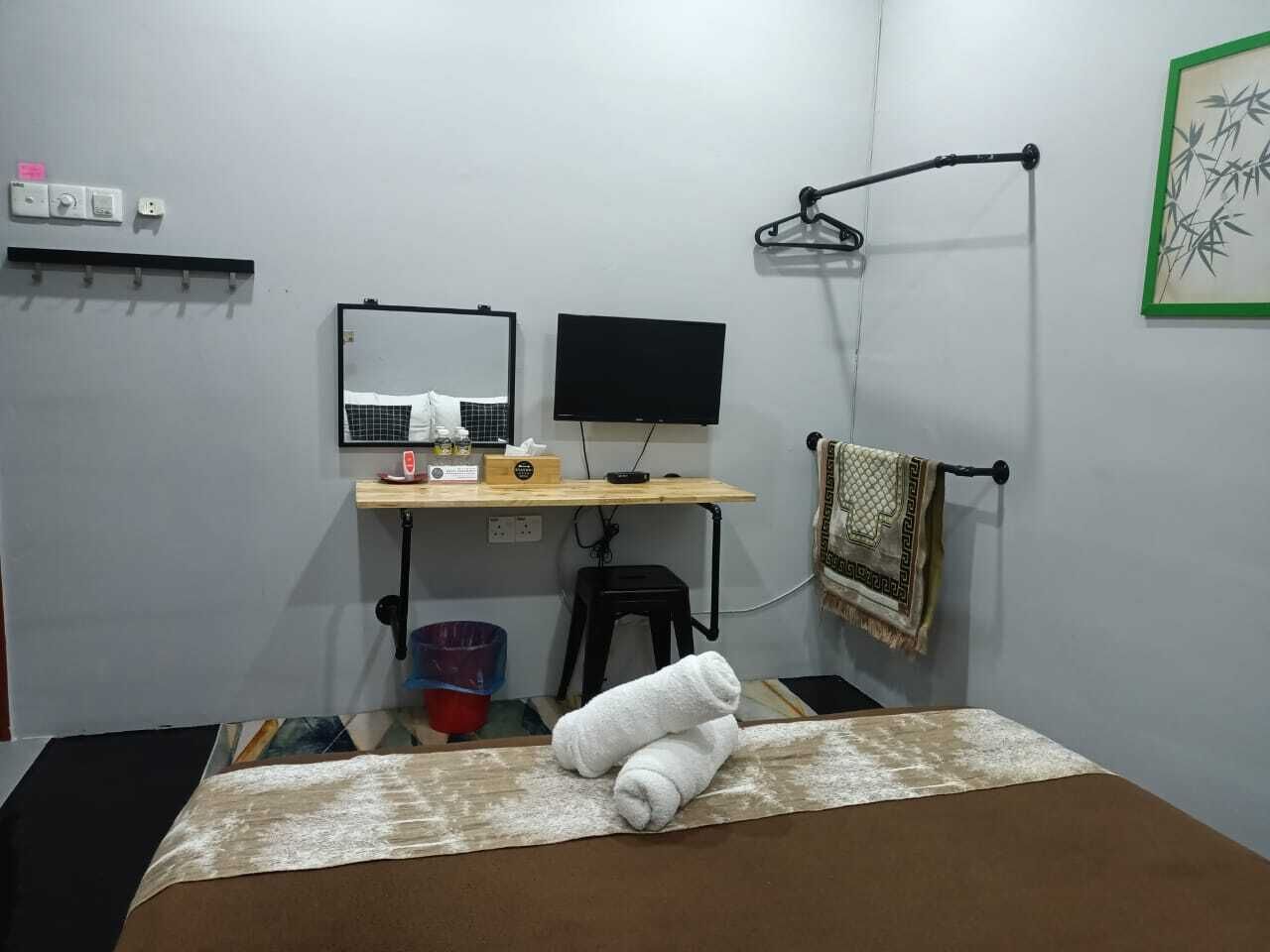 Una habitación pequeña con una cama, un escritorio con computadora y un espejo, una lámpara colgante y un perchero de toallas en la pared.