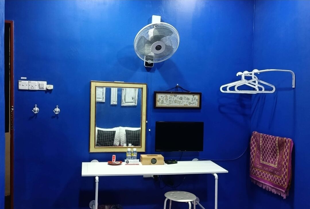 A bathroom with a blue wall, a white sink, a mirror, a fan, a black TV, and a towel rack.