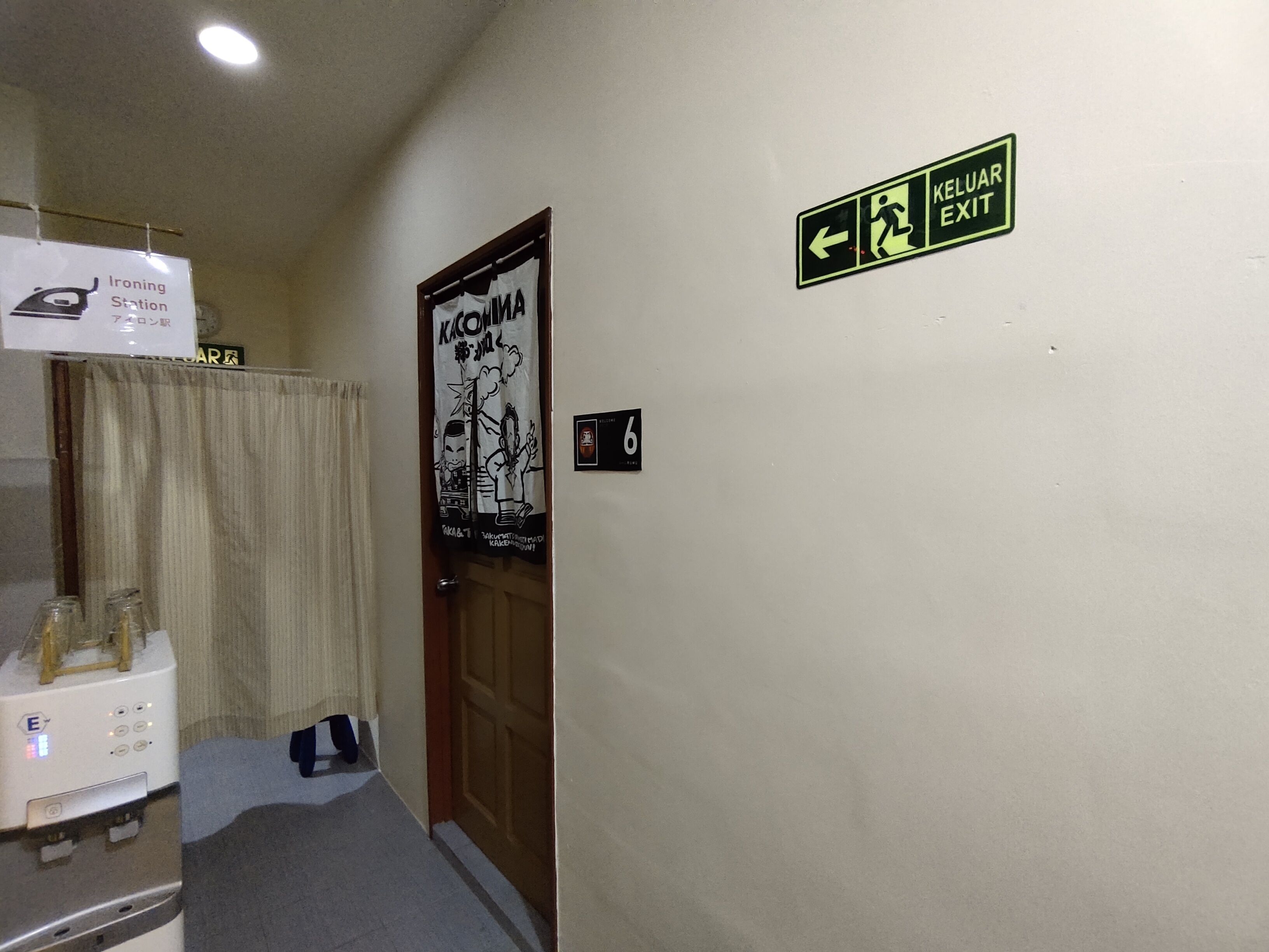 A hallway with a sign indicating an exit, a poster on the wall, and a door labeled with the number 6.