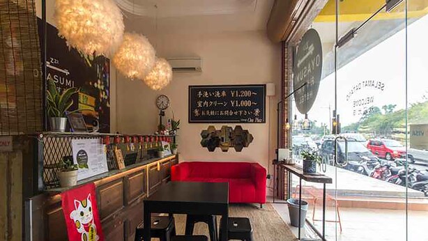 A restaurant interior with a black table, red sofa, and a menu board. - Oyasumi Hotel (Kulim)