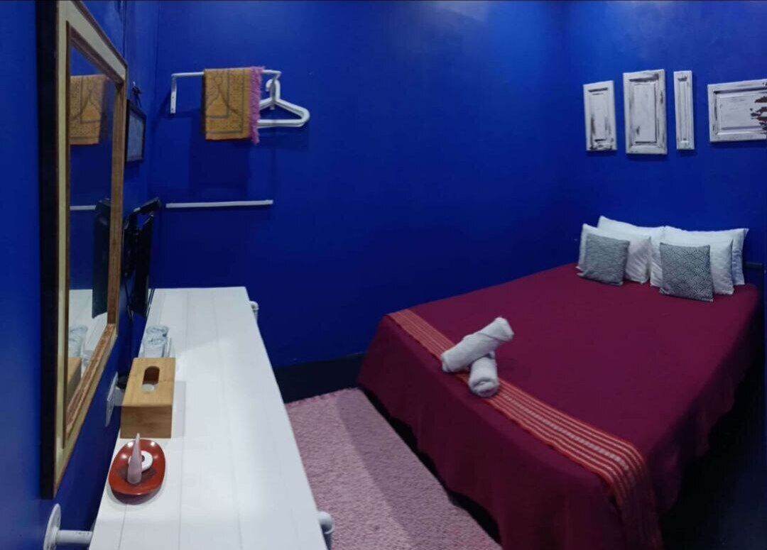 A room with a bed, a wooden bench, a mirror, and a towel rack.