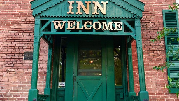 A brick building with a green awning and a sign that reads "INN WELCOME". - 1830s Historic Inn Ithaca NY, Room 8 (Lansing)