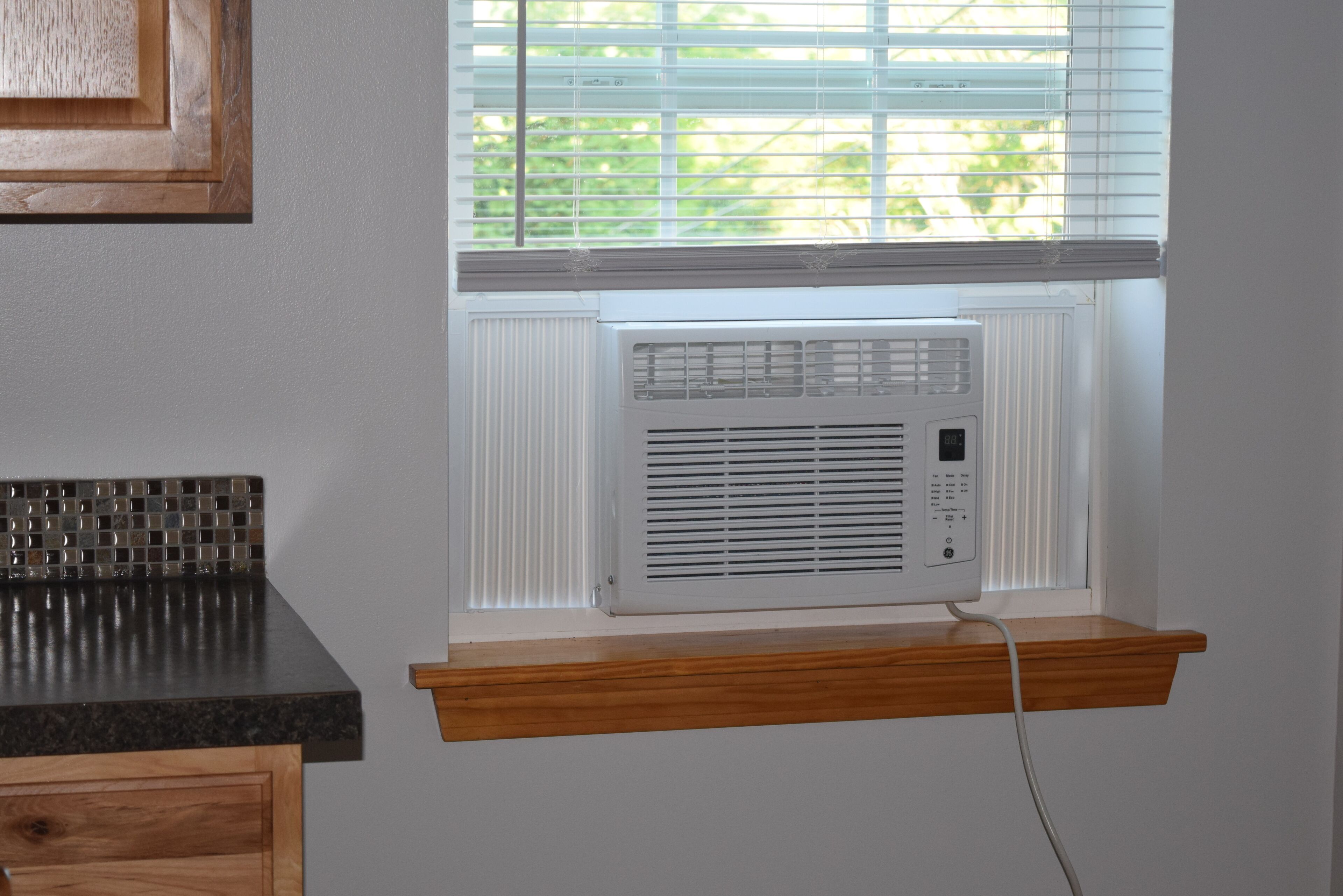 A kitchen with a built-in air conditioner, a wooden countertop, and a window with blinds.