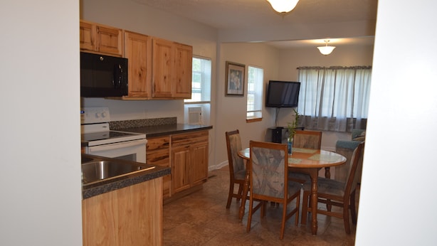 A kitchen with wooden cabinets, a microwave, stove, and a dining area with chairs and a table. - Cattaraugus, Your home away from home (Cattaraugus)