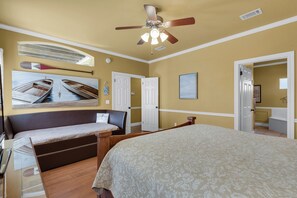 Ein Schlafzimmer mit einem großen Bett, einem kleineren Bett, einem Deckenventilator und einem Gemälde von Booten an der Wand.