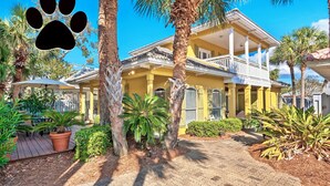 A two-story yellow building with a balcony, surrounded by palm trees and potted plants. - Renovated Pet Friendly Home-Private Beach Access (Destin)