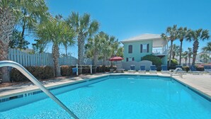 A swimming pool with a metal ladder, surrounded by palm trees and a white fence. There are lounge chairs and a red umbrella near the pool. - Renovated Pet Friendly Home-Private Beach Access (Destin)