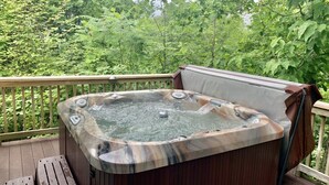 A hot tub on a wooden deck with a view of dense greenery.