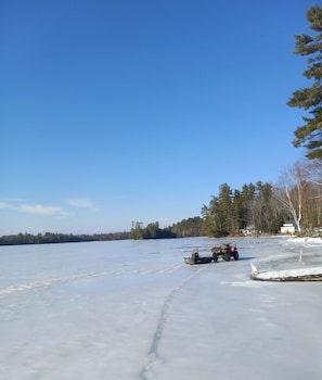 Un lago helado con una pequeña embarcación y un vehículo todo terreno sobre el hielo.