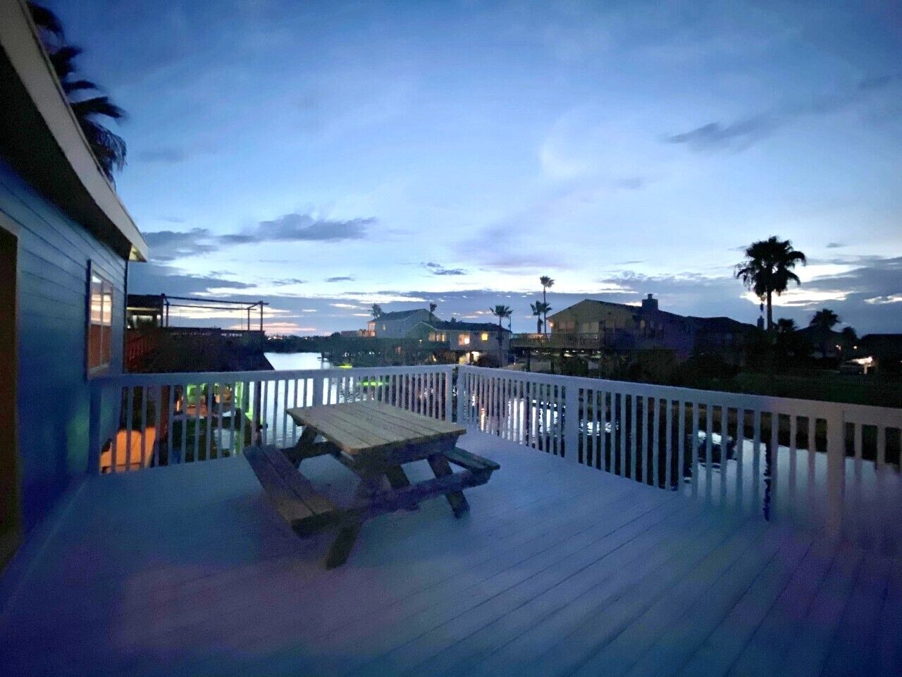 Une terrasse en bois avec une table de pique-nique, donnant sur une étendue d’eau, avec des bâtiments en arrière-plan.