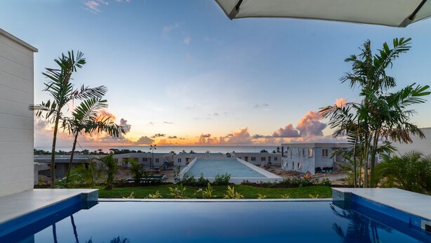Ein Pool mit Blick auf einen Resortkomplex und das Meer bei Sonnenuntergang.