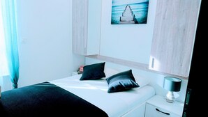 A hotel room with a bed, pillows, a bedside table with a lamp, and a painting of a pier on the wall.