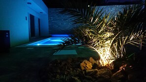 Un área de piscina moderna al aire libre con un muro de piedra y plantas de palma.