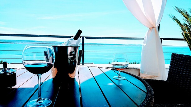 A table with two wine glasses and a bottle, overlooking a body of water.