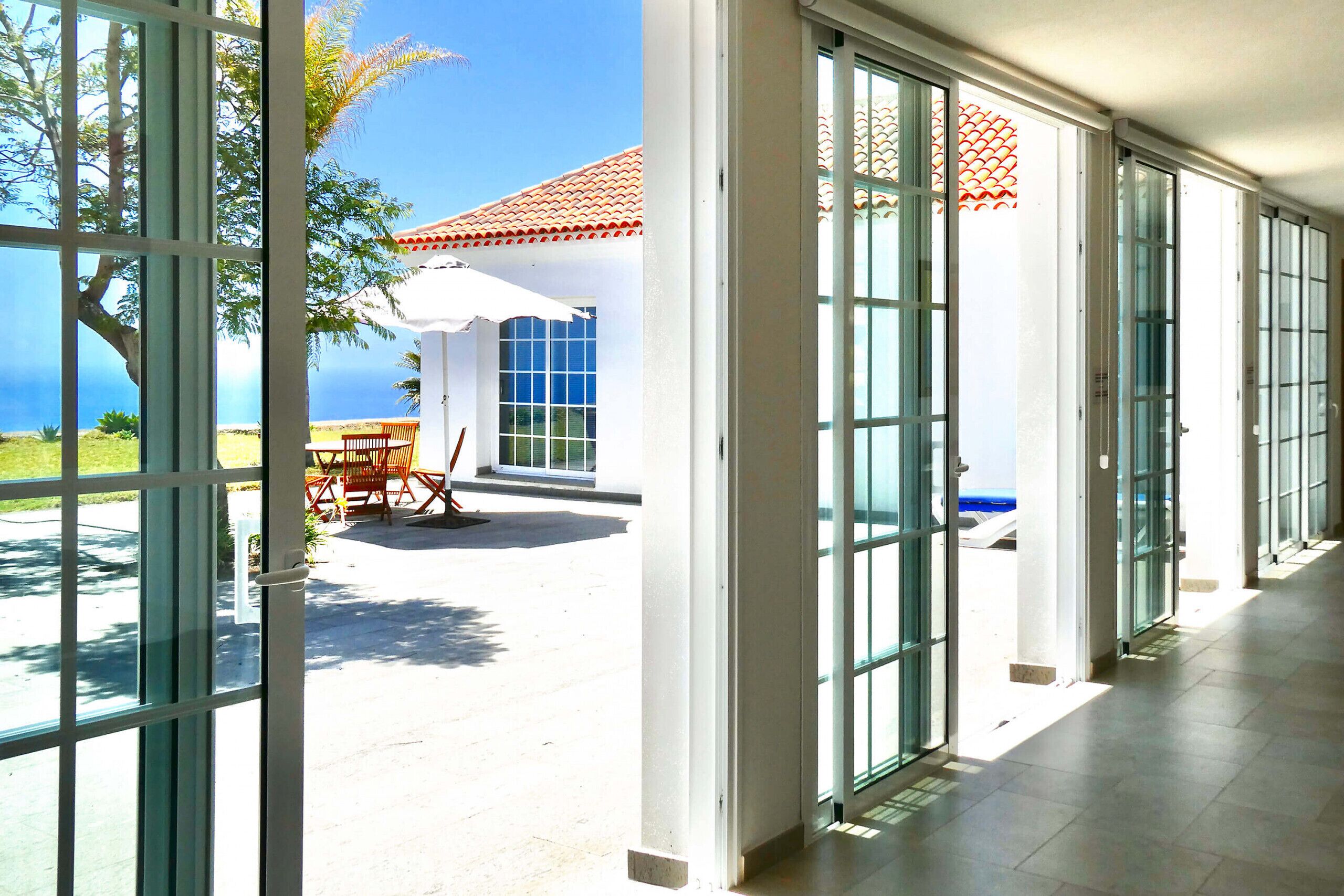 Un couloir d’hôtel avec de grandes portes vitrées donnant sur un patio aménagé avec du mobilier d’extérieur et offrant une vue sur la mer.