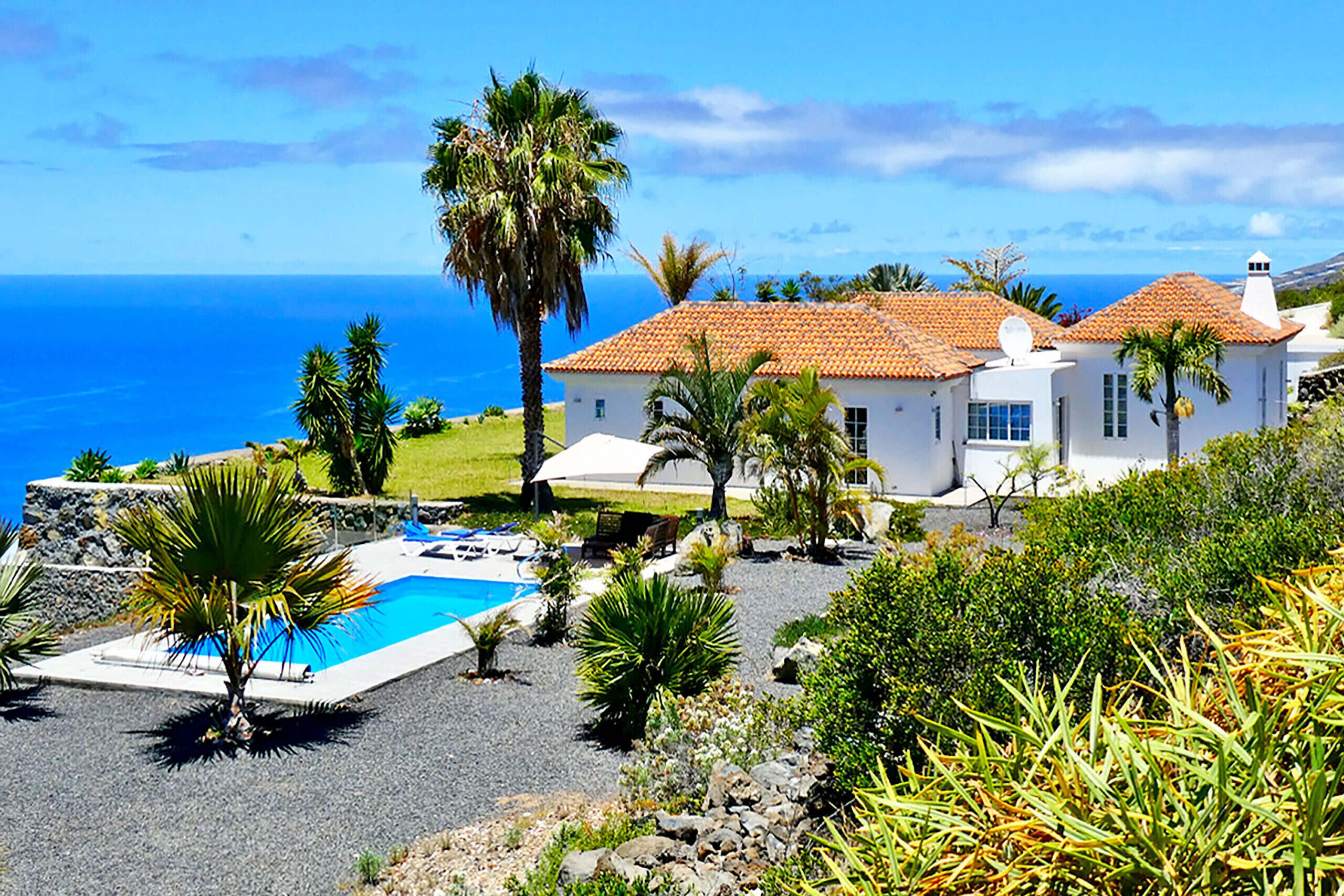 Una casa costera con piscina, rodeada de palmeras y vista al mar.
